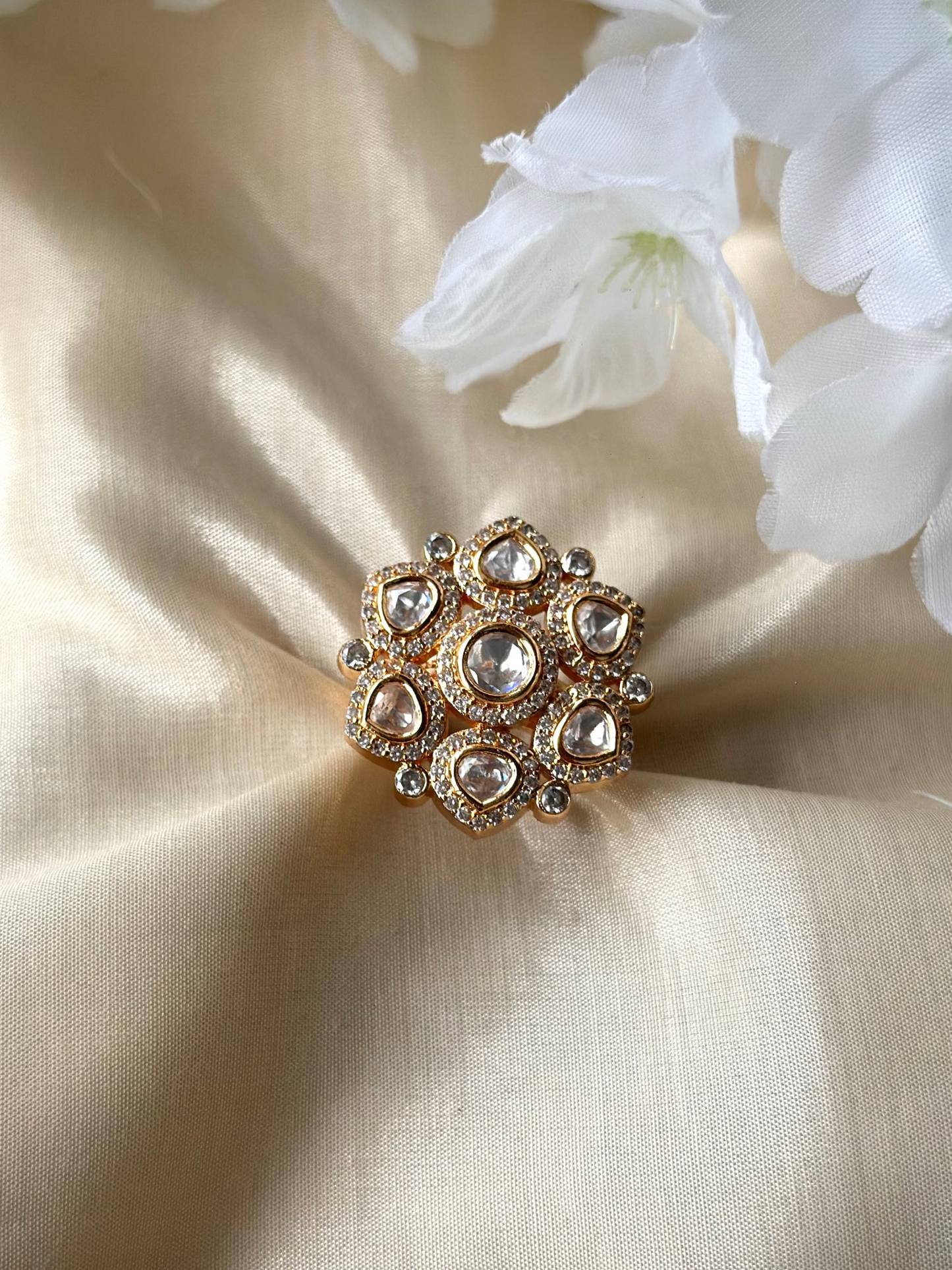 Gold ring with gemstones on a beige fabric background with white flowers