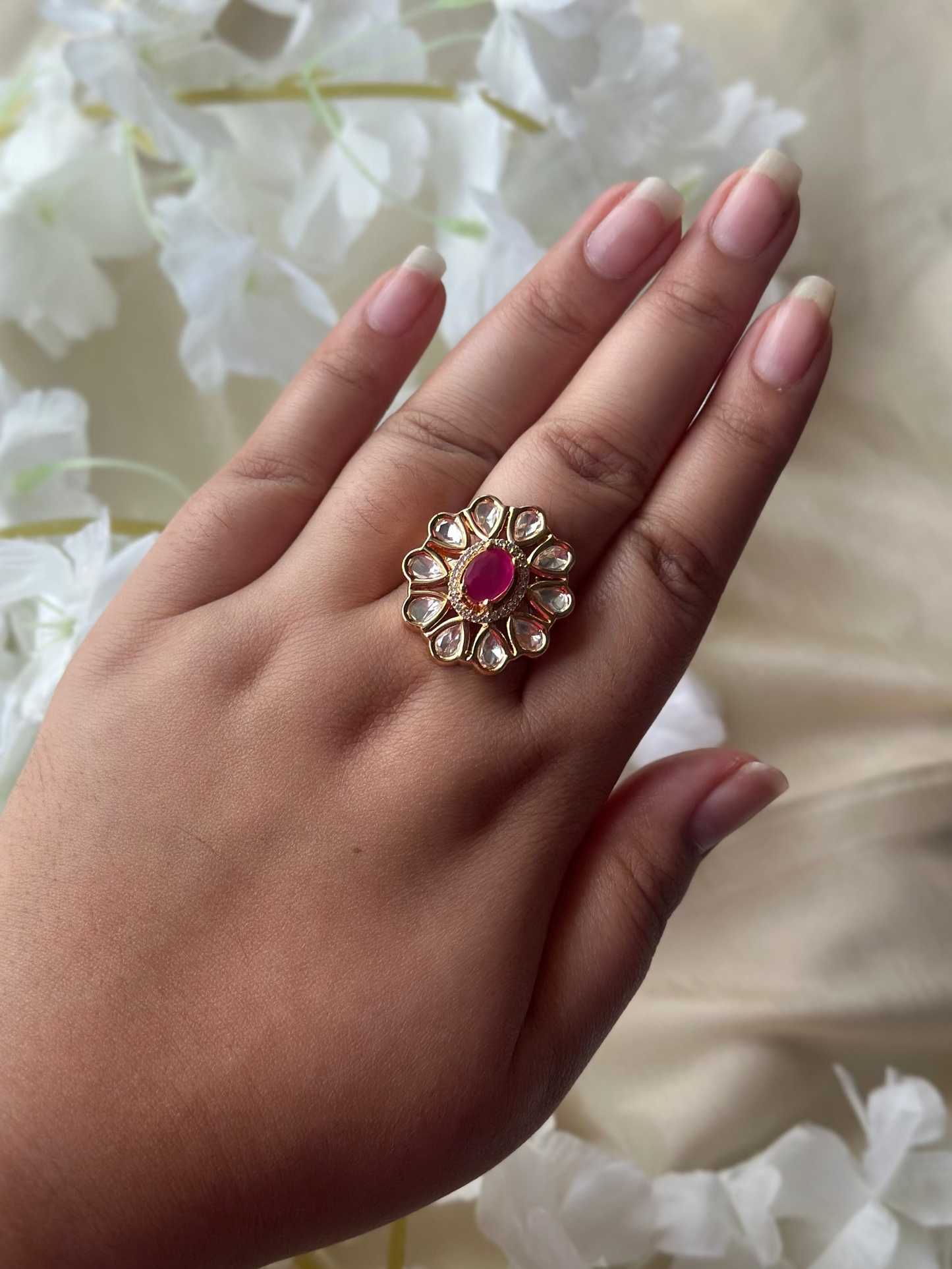 Hand wearing a decorative ring with a red gemstone against a floral background