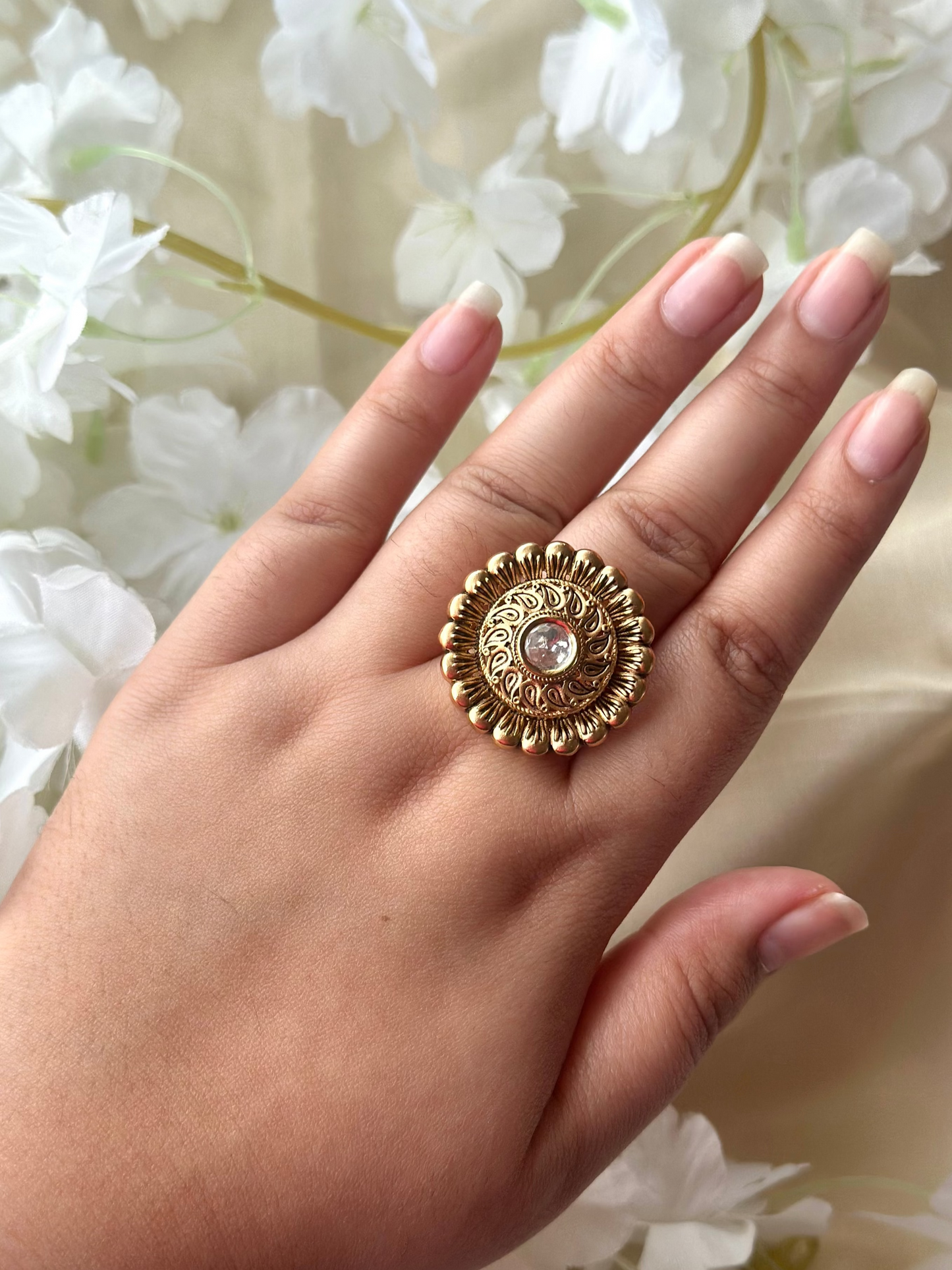 Hand wearing a gold ring with a decorative design against a floral background