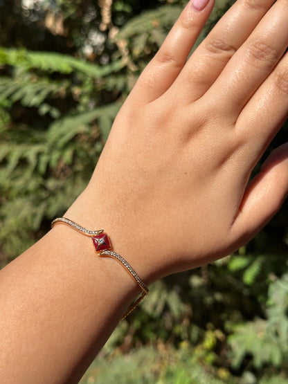 A gold bracelet with a diamond clasp on a person's wrist, displayed against a leafy background.