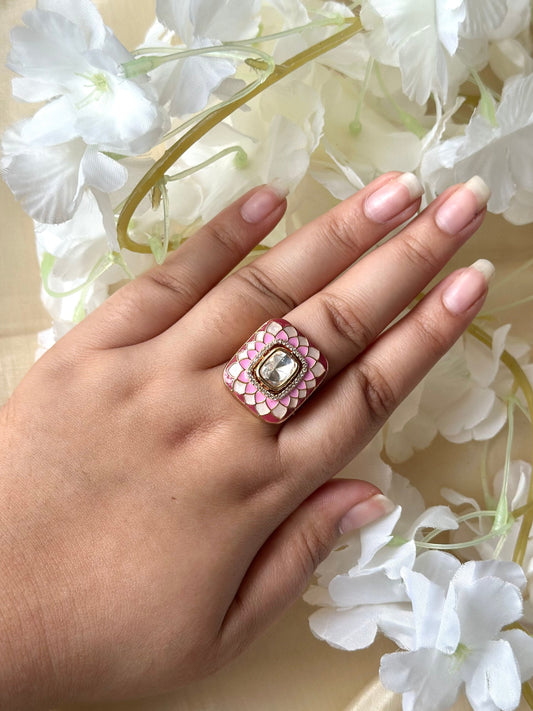 Hand wearing a decorative ring with pink stones and a clear gemstone, against a floral background.