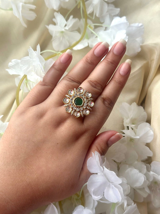 Hand wearing a decorative ring with a green gemstone against a floral background
