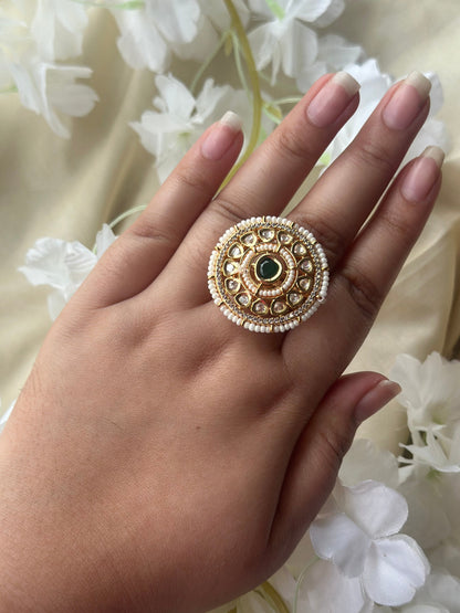 Hand wearing a gold ring with a green gemstone against a floral background