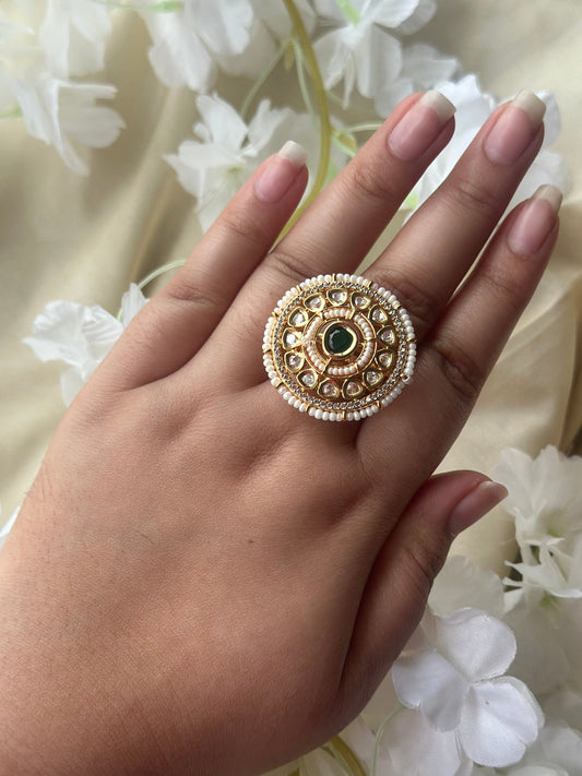 Hand wearing a gold ring with a green gemstone against a floral background