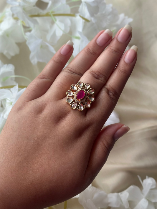Hand wearing a decorative ring with a red gemstone against a floral background