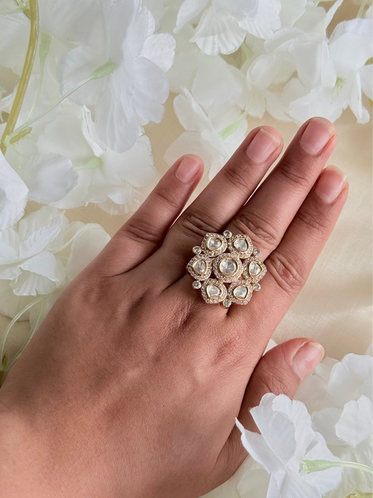 Hand wearing a decorative ring with white flowers in the background